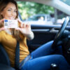 Driving school. Young beautiful woman successfully passed driving school test. Female smiling and holding driver's license. Girl with driving license.