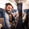 Happy man traveling by plane and turning towards the camera while looking at it.