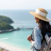 Young beautiful Asian woman with backpack solo travel on tropical island mountain peak in summer sunny day. Cheerful female relax and enjoy outdoor lifestyle in summer beach holiday vacation trip