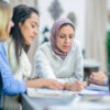 A beautiful Muslim woman wearing a hijab is leading a discussion meeting with her multi ethnic group of entrepreneurs in an office.