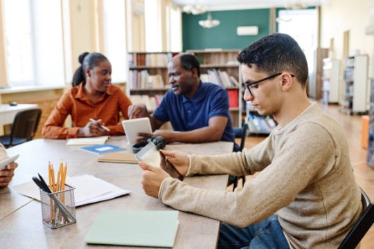 Young Middle Eastern student and his Black classmates attending lesson for immigrants in library using digital tablets