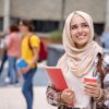 Portrait of a thoughtful female Muslim student smiling in college and holding a cup of coffee while smiling - education concepts