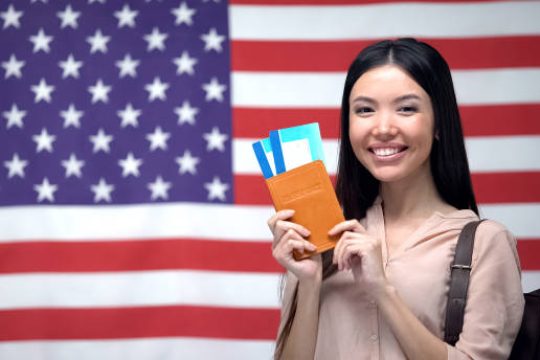 Excited woman holding passport and flight tickets against USA flag background